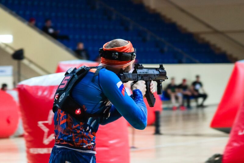 Боец LASERWAR в защитной экипировке целится из оружия.